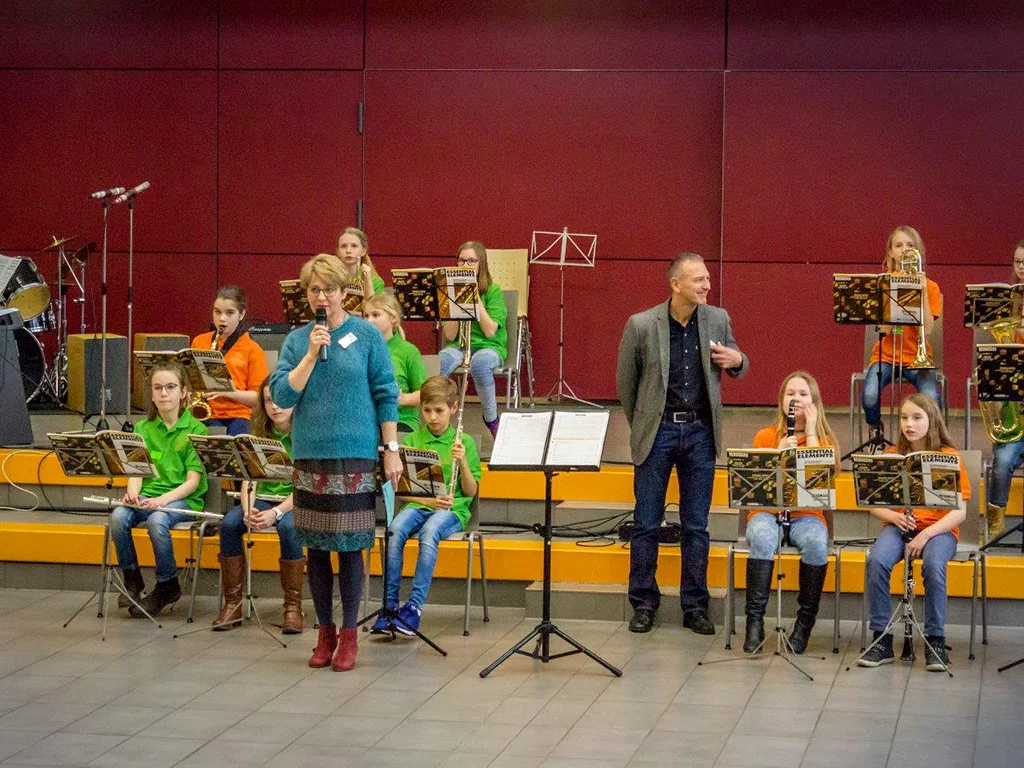 Die Bläserklasse spielt auf der Bühne, ein Lehrer dirigiert.